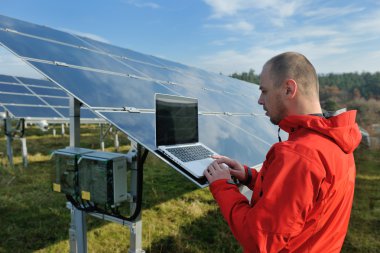 Engineer using laptop at solar panels plant field clipart