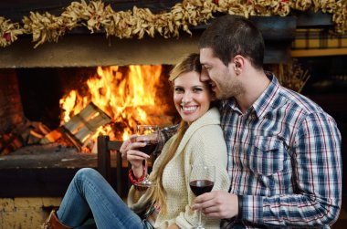 Young romantic couple sitting on sofa in front of fireplace at h clipart