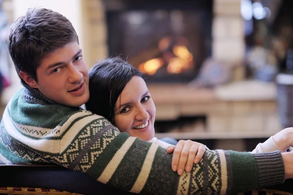 Young romantic couple sitting on sofa in front of fireplace at h — Stock Photo, Image