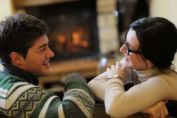 Young romantic couple sitting on sofa in front of fireplace at h — Stock Photo, Image