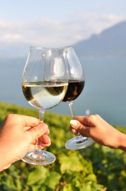 Two hands holding wineglases against vineyards in Lavaux region, clipart
