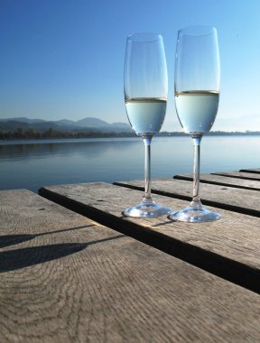 Two champagne glasses against a lake