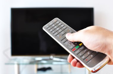 Remote control in the hand against TV screen