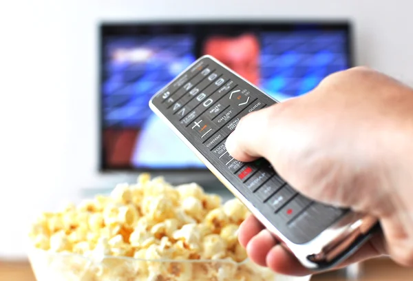 Controle remoto na mão contra pop-milho e TV-set — Fotografia de Stock