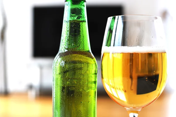 Un vaso de cerveza y una botella contra el televisor — Foto de Stock