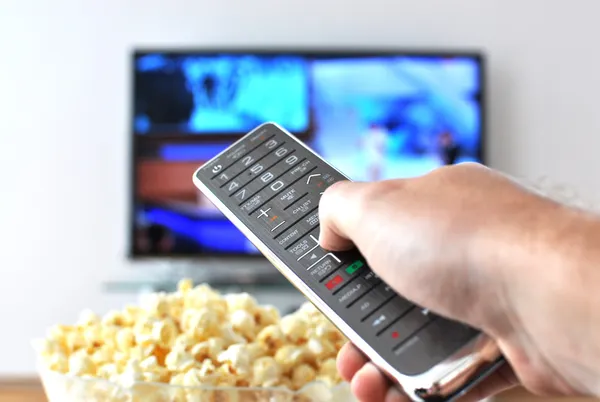 Control remoto en la mano contra el pop-corn y el televisor — Foto de Stock