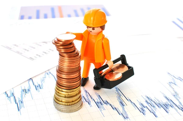 Un pequeño trabajador construyendo una pirámide de monedas contra informes financieros —  Fotos de Stock
