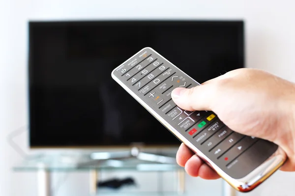 Controle remoto na mão contra tela de TV — Fotografia de Stock