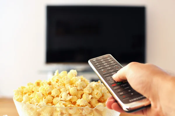 Control remoto en la mano contra el pop-corn y el televisor —  Fotos de Stock