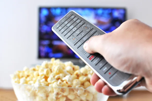 Пульт дистанционного управления в руке против попкорна и телевизора — стоковое фото