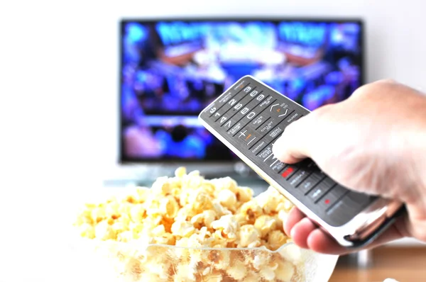 Controle remoto na mão contra pop-milho e TV-set — Fotografia de Stock