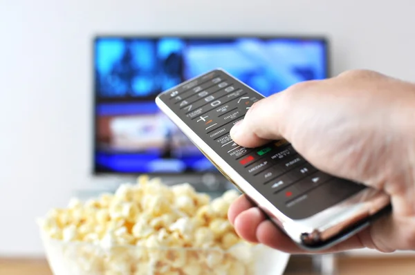 Пульт дистанційного керування в руці проти попкорну і телевізора — стокове фото