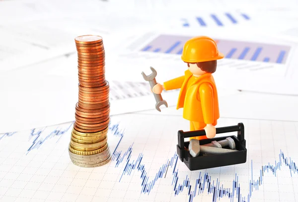 Un pequeño trabajador en una pirámide de monedas contra informes financieros —  Fotos de Stock