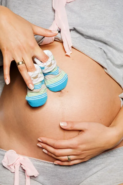Těhotná žena drží dětské boty — Stock fotografie