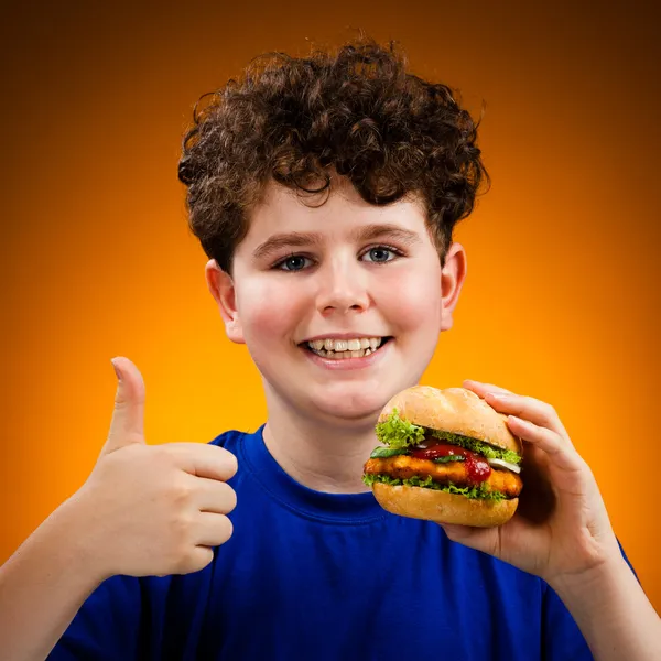 Menino comendo sanduíche grande mostrando sinal OK — Fotografia de Stock