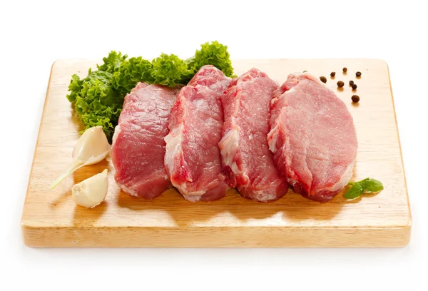 Nyers sertéshús daraboló asztalon és zöldségeken — Stock Fotó