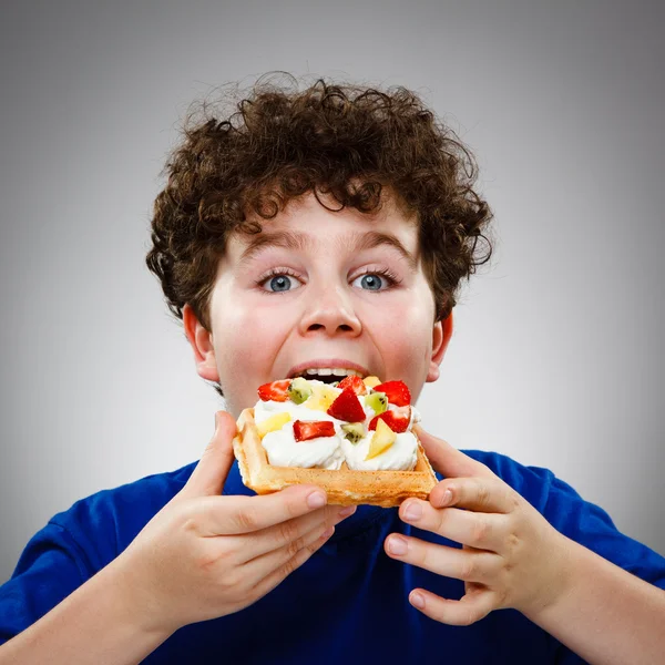 Junge isst Kuchen mit Sahne und Früchten — Stockfoto