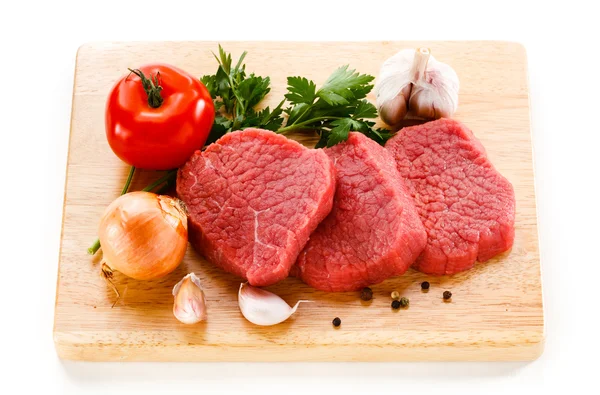 Carne de bovino em bruto sobre tábua de corte e produtos hortícolas — Fotografia de Stock