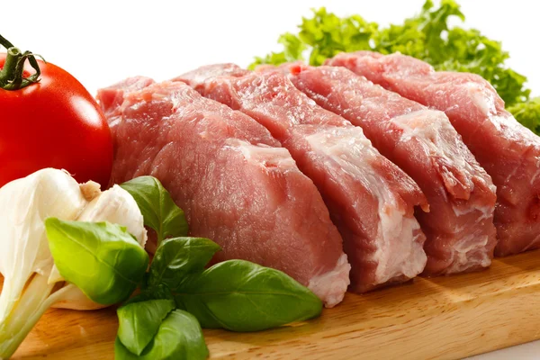 Nyers sertéshús daraboló asztalon és zöldségeken — Stock Fotó