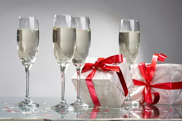Sklenice šampaňského, dárky s červený pásek a luky — Stock fotografie