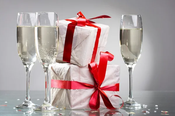 Glasses of champagne, gifts with red tapes and bows — Stock Photo, Image