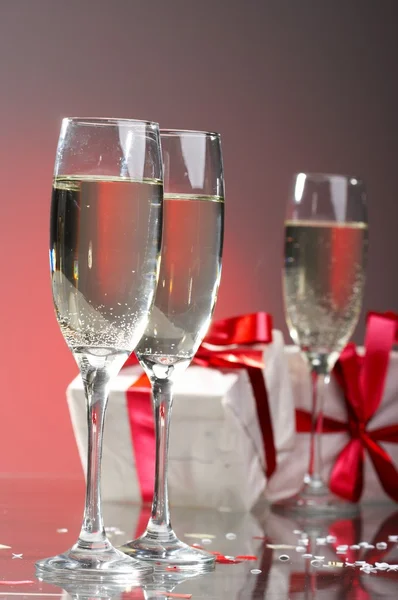 Glazen van champagne, geschenken met rode tapes en strikken — Stockfoto