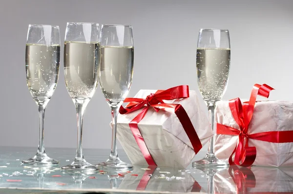 Glasses of champagne, gifts with red tapes and bows — Stock Photo, Image