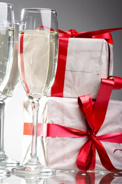 Sklenice šampaňského, dárky s červený pásek a luky — Stock fotografie