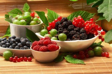 Berries in plates, on a table, among green leaves clipart