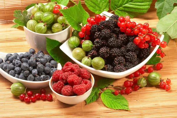 Berries in plates, on a table, among green leaves — Stock Photo, Image