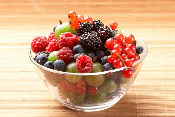 Owoce wymieszać w szklanym pojemniku, na stole ze słomy — Zdjęcie stockowe