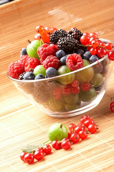 Owoce wymieszać w szklanym pojemniku, na stole ze słomy — Zdjęcie stockowe