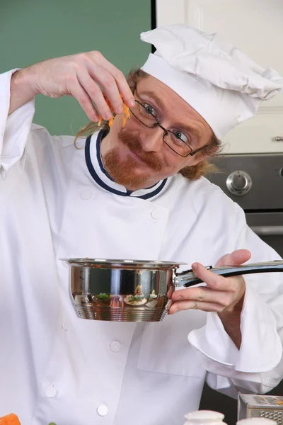 Grappige jonge chef-kok toevoegen wortelen in de pot — Stockfoto