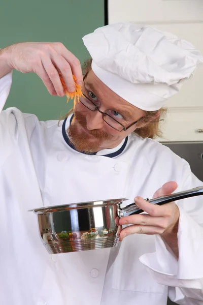 Legrační mladé šéfkuchaře přidat mrkev v hrnci — Stock fotografie