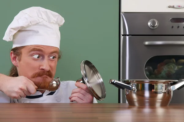 Legrační mladý kuchař divně při pohledu na hrnec — Stock fotografie