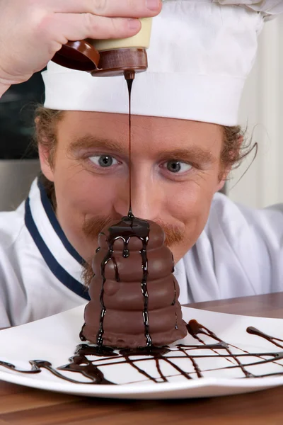 Funny young chef added chocolate sauce at piece of cake — Stock Photo, Image