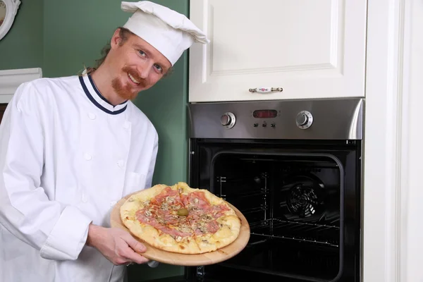 Молодой шеф-повар с итальянской пиццей на кухне — стоковое фото