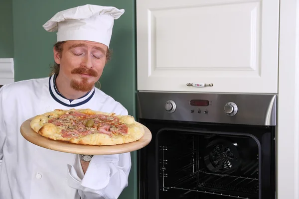 Joven chef oliendo pizza italiana en la cocina — Foto de Stock