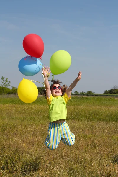 Happy little girl jumping with balloons on meadow — Stock Photo, Image
