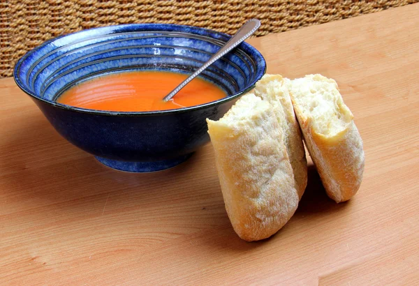 Rouleau de pain et bol à soupe bleue avec soupe aux tomates rouges — Photo