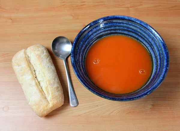 Rolo de pão e uma tigela de sopa azul com sopa de tomate vermelho — Fotografia de Stock