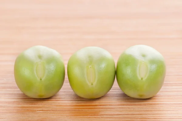 Three fresh green peas on wooden background — Stock Photo, Image