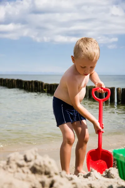 Pojken gräva i sanden på stranden — Stockfoto
