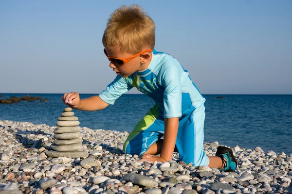 Chico en traje de baño construyendo pila de piedra en la playa de guijarros — Foto de Stock