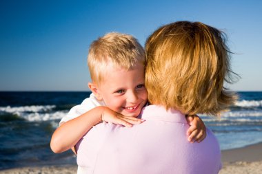 Boy hugging mother on beach clipart