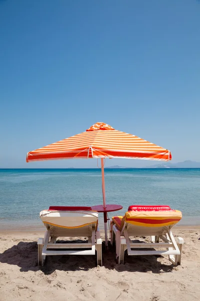 Два шезлонга под зонтиком на пляже в солнечный день — стоковое фото