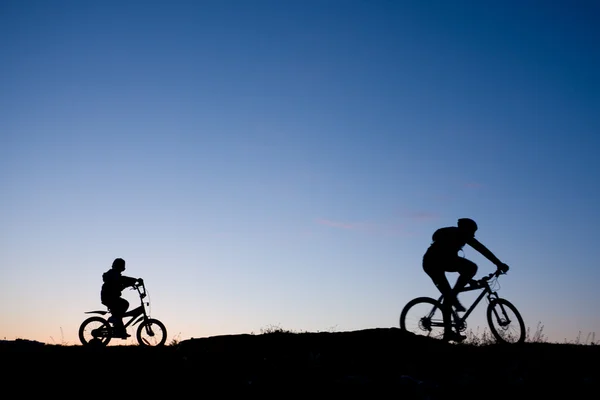 两个骑自行车的人反对日落-父亲和儿子的剪影 — 图库照片