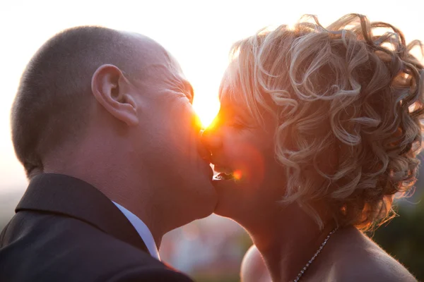 Bruid en bruidegom kussen bij zonsondergang — Stockfoto