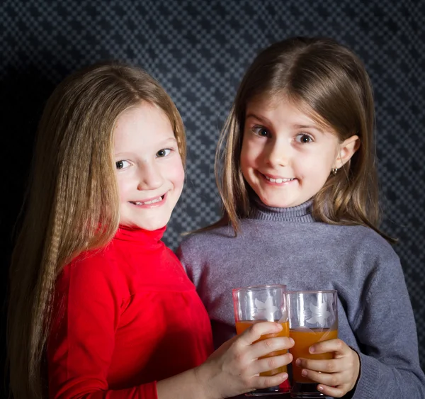 Due bambine che tengono i bicchieri e bevono frutta arancione — Foto Stock