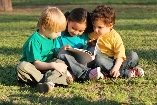Skupina dětí s knihou na trávě v parku — Stock fotografie
